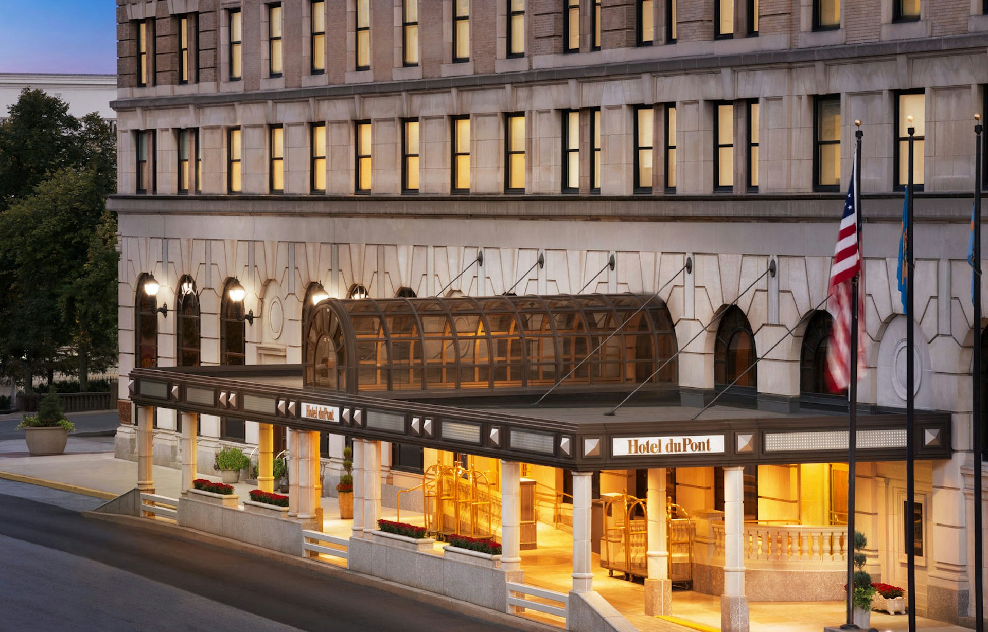 A large white stone building with many windows. There's an arched glass-and-steel canopy over the entrance 