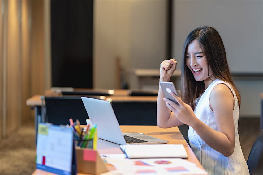 企业和生活方式概念，偶然套装的亚洲女商人很高兴在完成在线购物通过智能手机应用或技术膝上型计算机在现代办公室