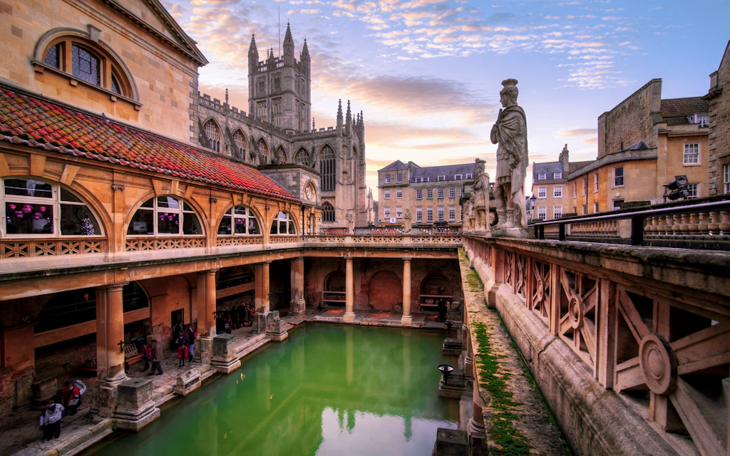 A large green open-air rectangular pool of water surrounded by sandstone walls. A huge cathedral building overlooks the scene