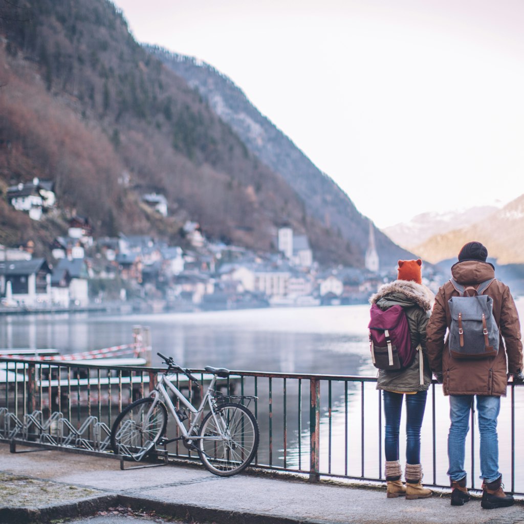 Young couple at winter mountain village, standing on bridge and looking at the Hallstatt lake.