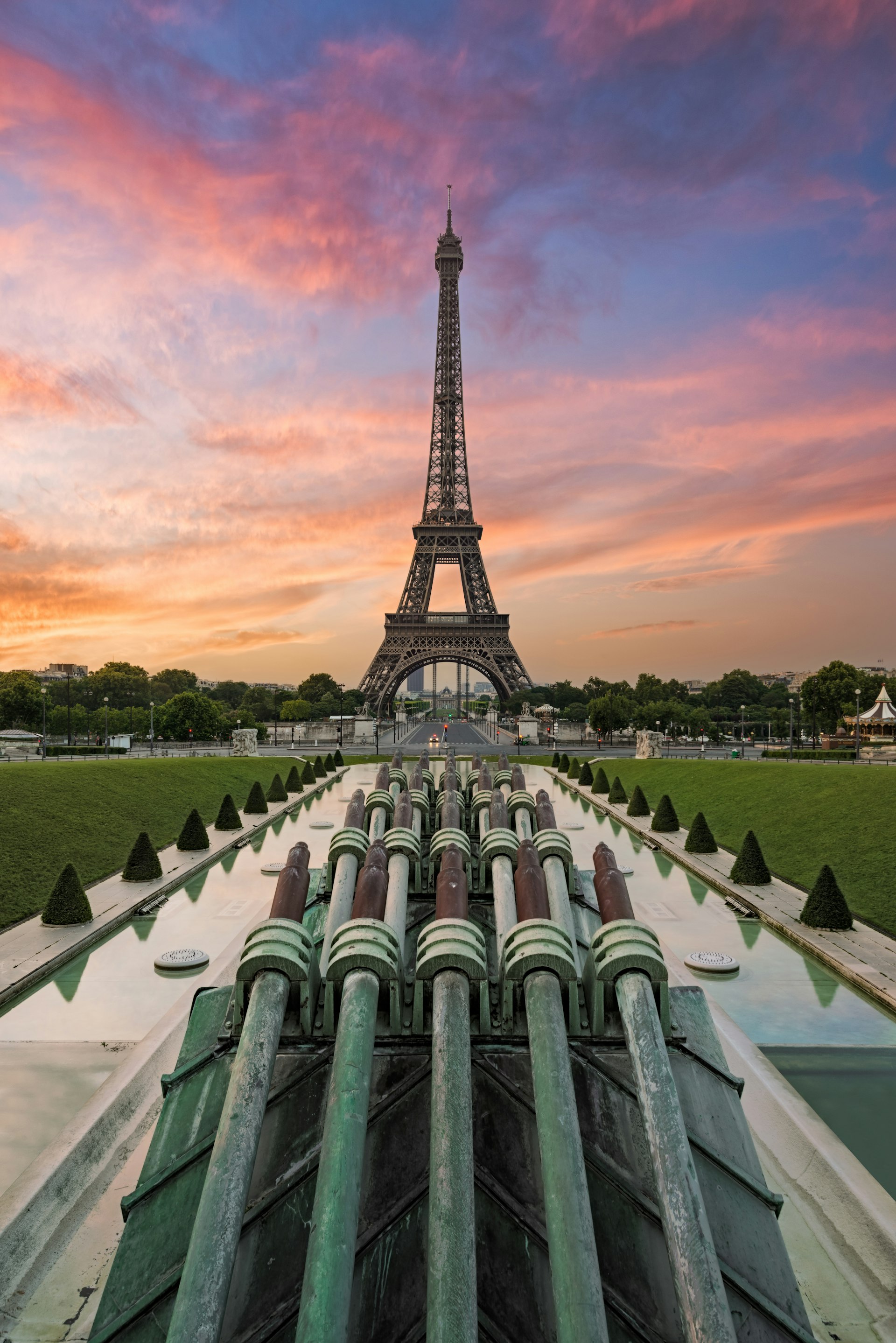 The Eiffel Tower at sunrise. The sky is blue and pink behind the structure.