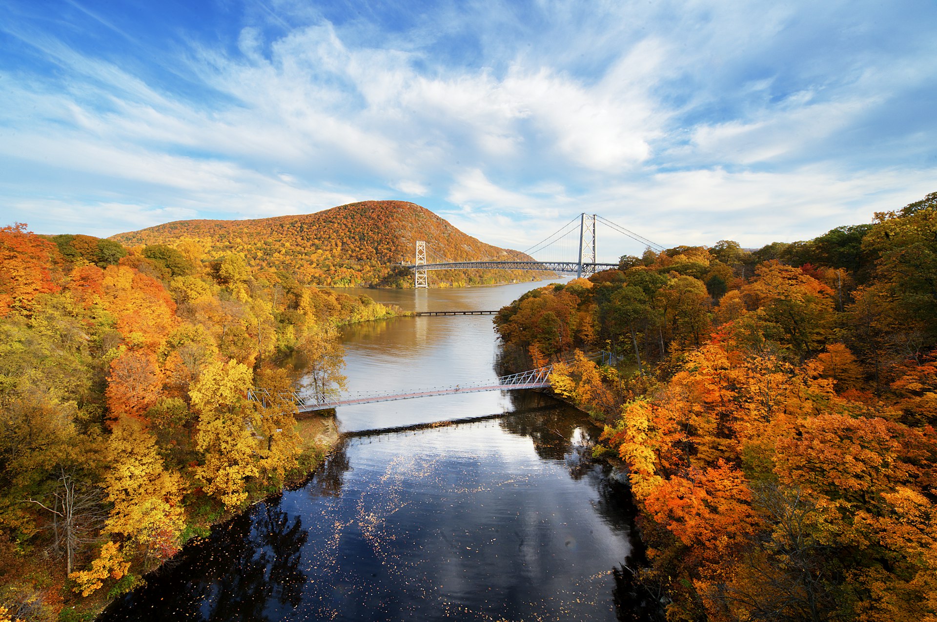 A river winds through lush fall foliage with a bridge in the distance