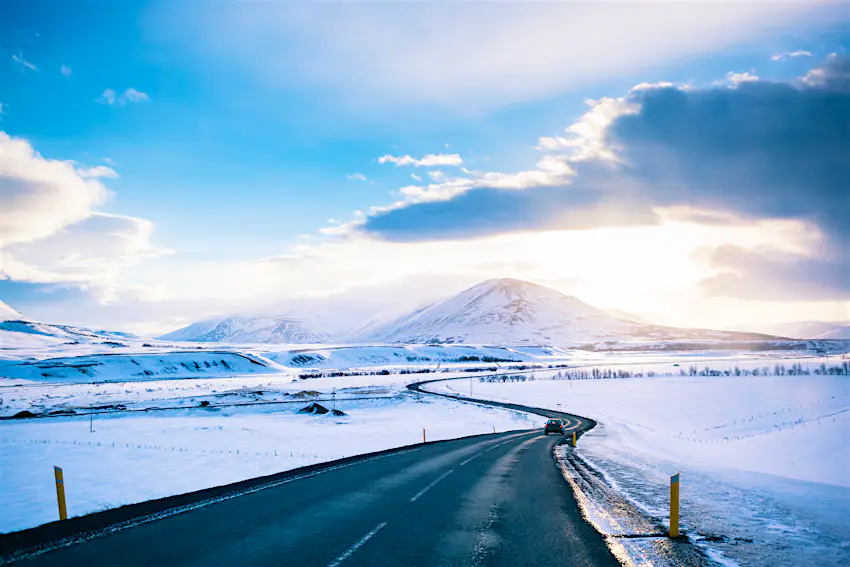 Winter Road at iceland A car drives on a winter road near Akureyri, Iceland. The black road is surrounded by miles of snowy terrain. Mountains are visible in the distance.