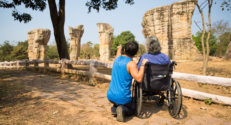 A man wearing blue singlet and black sport pants takes his old mother on wheelchair to see the strange rock formation of Mo Hin Khao (Thailand's Stonehenge) in Chaiyaphum Province, Thailand.