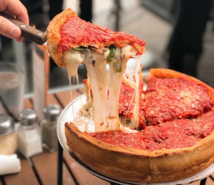 Taking a slice of Chicago-style deep dish cheese pizza with tomato sauce.