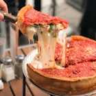 Taking a slice of Chicago-style deep dish cheese pizza with tomato sauce.