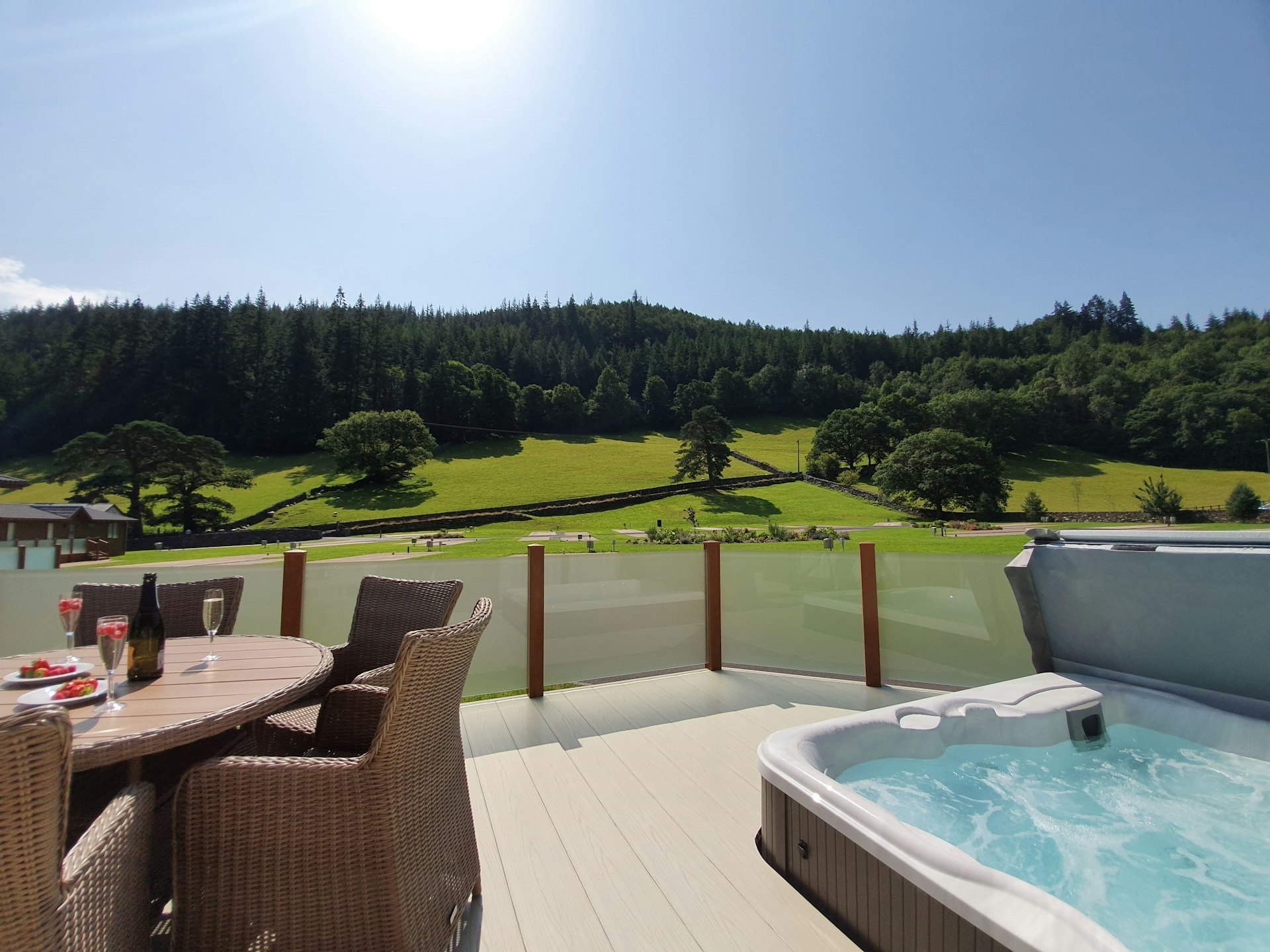 An outside deck with garden furniture and a hot tub, with rolling green fields in the background