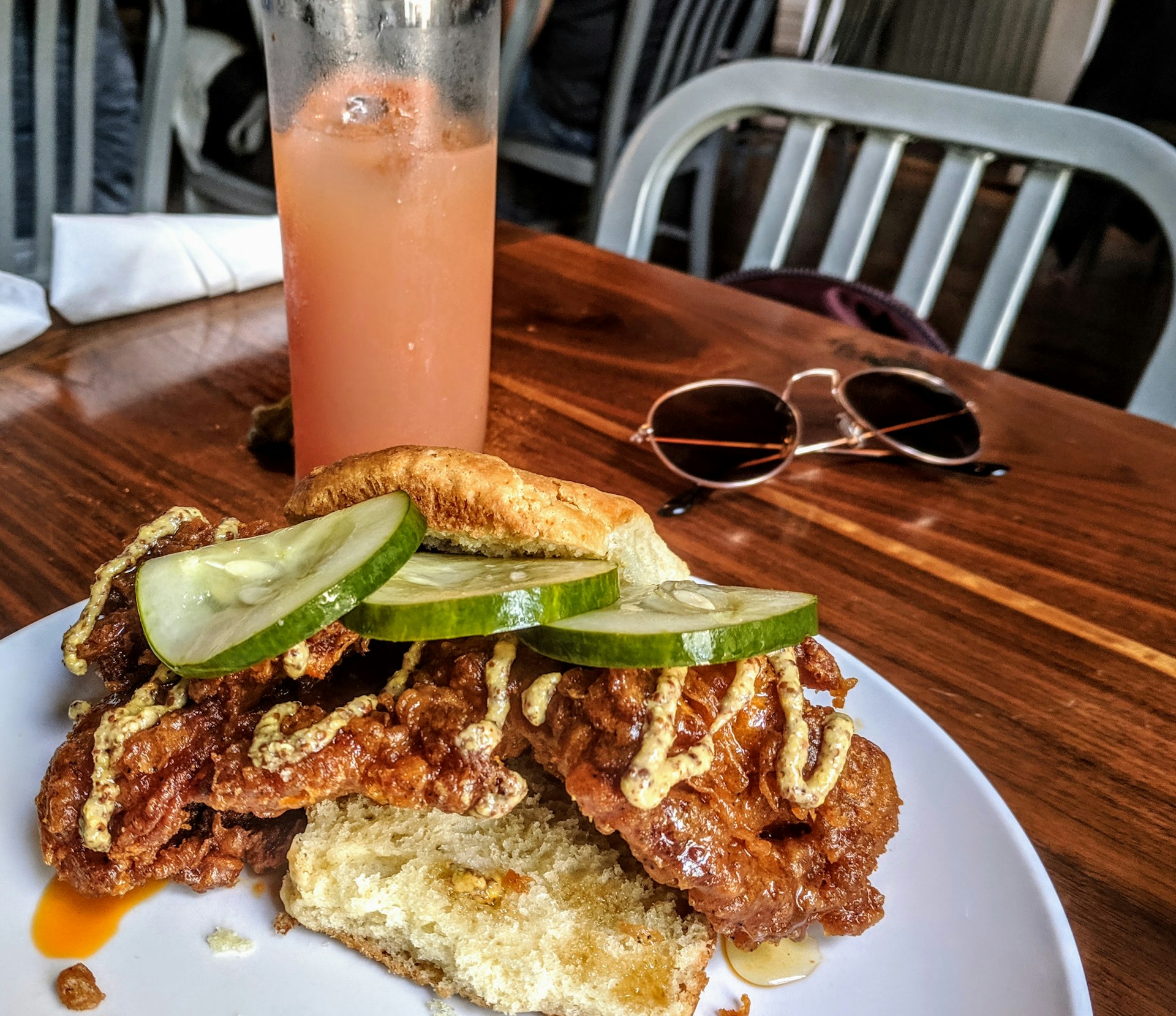 A plate full of food including hot chicken on bread with gherkins on top, and an orange-colored smoothie