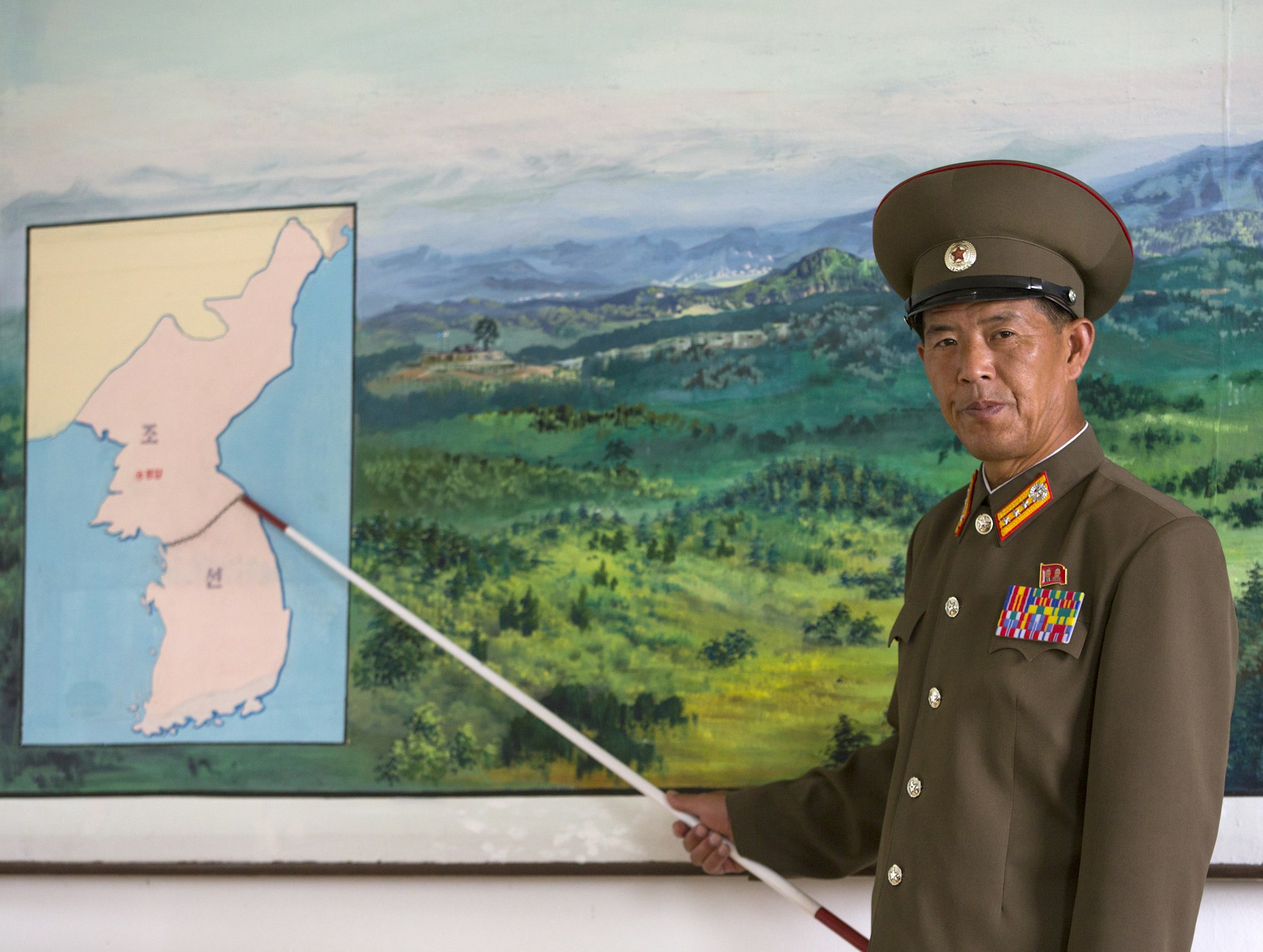 A stern-faced colonel using a stick to point to a map of the DMZ splitting North Korea