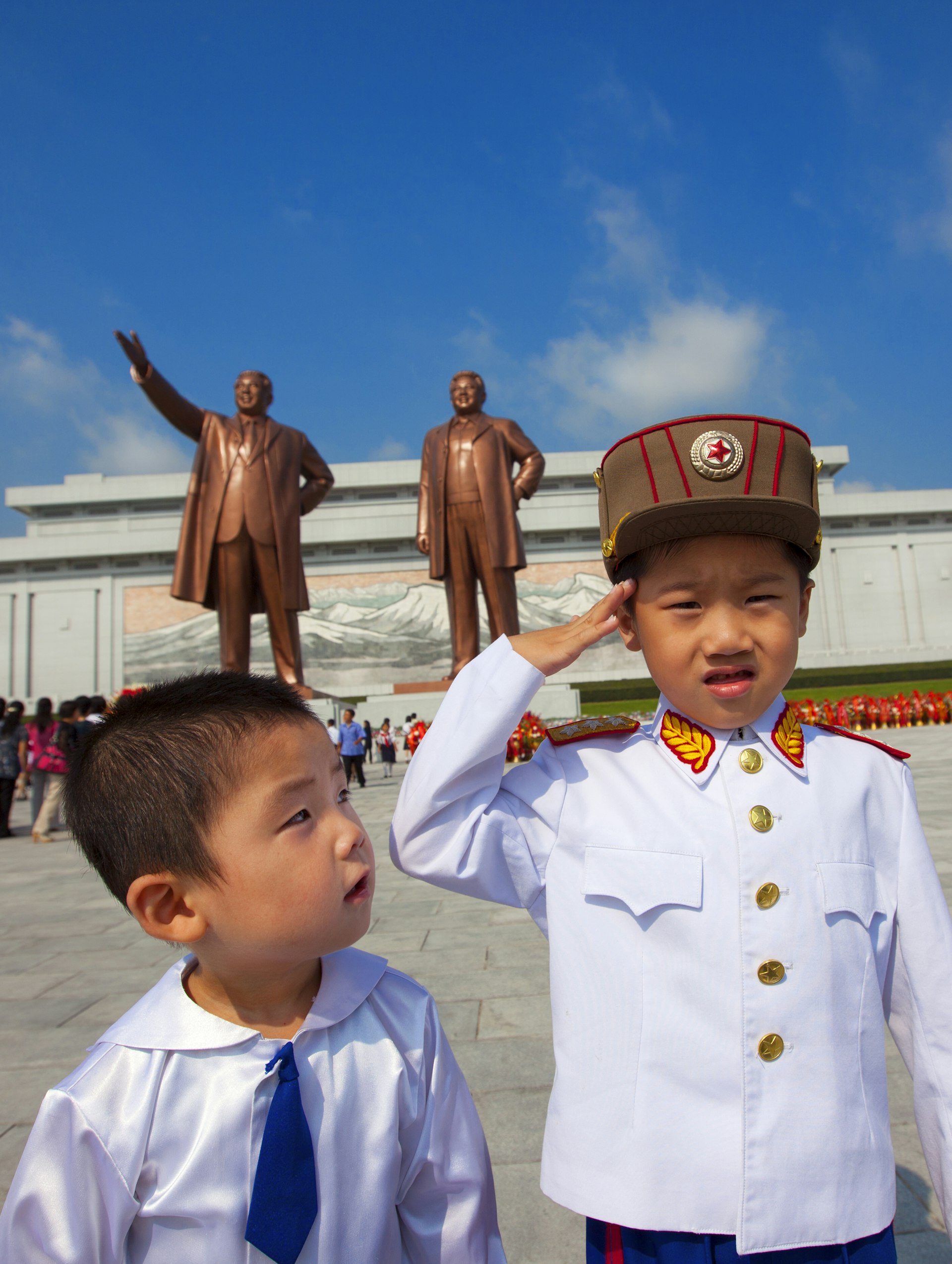 Two young boys in front of giant statues of  Kim Il Sung and Kim Jong-il in Grand Monument of Mansu Hill.