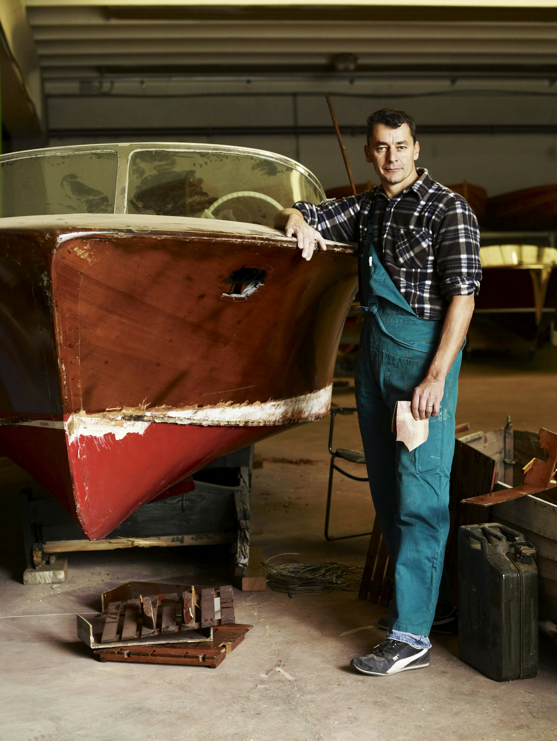 A man poses next to a classic cedar boat, sandpaper in hand