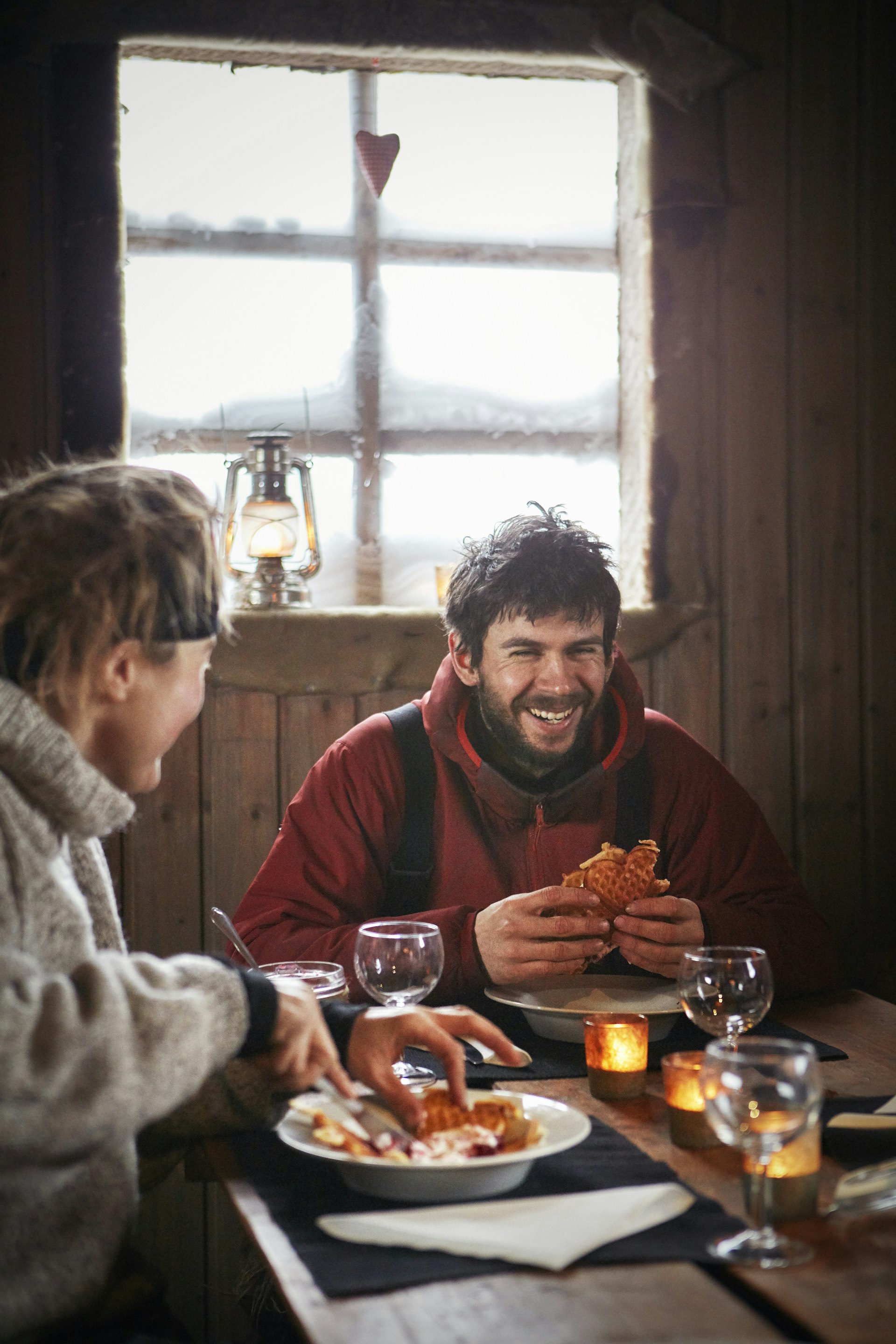 A man laughs while eating waffles inside a cabin