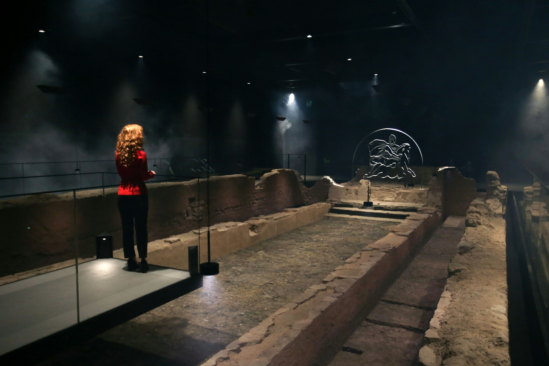 An employee poses alongside a reconstruction of the Roman Temple of Mithras. It is dark but the stone is illuminated by warm light.