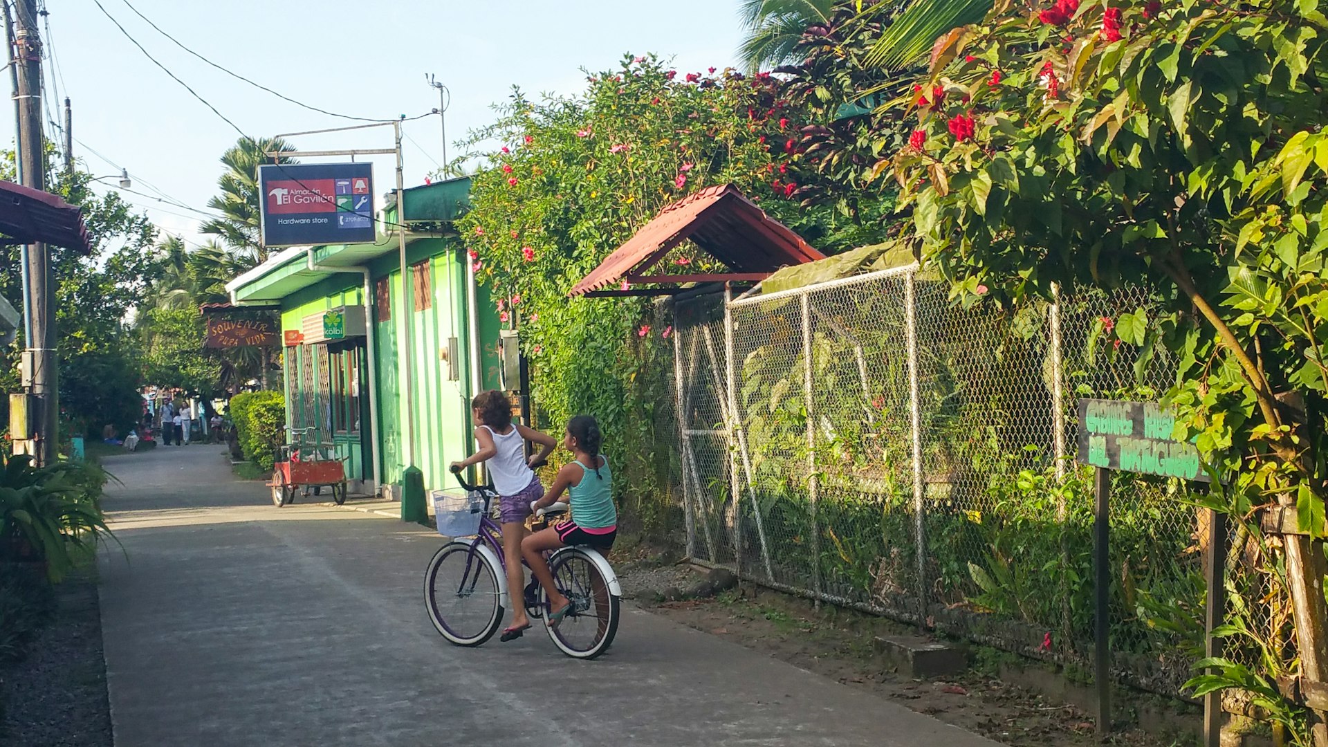 Two girls pedal down the main road of Tortuguero