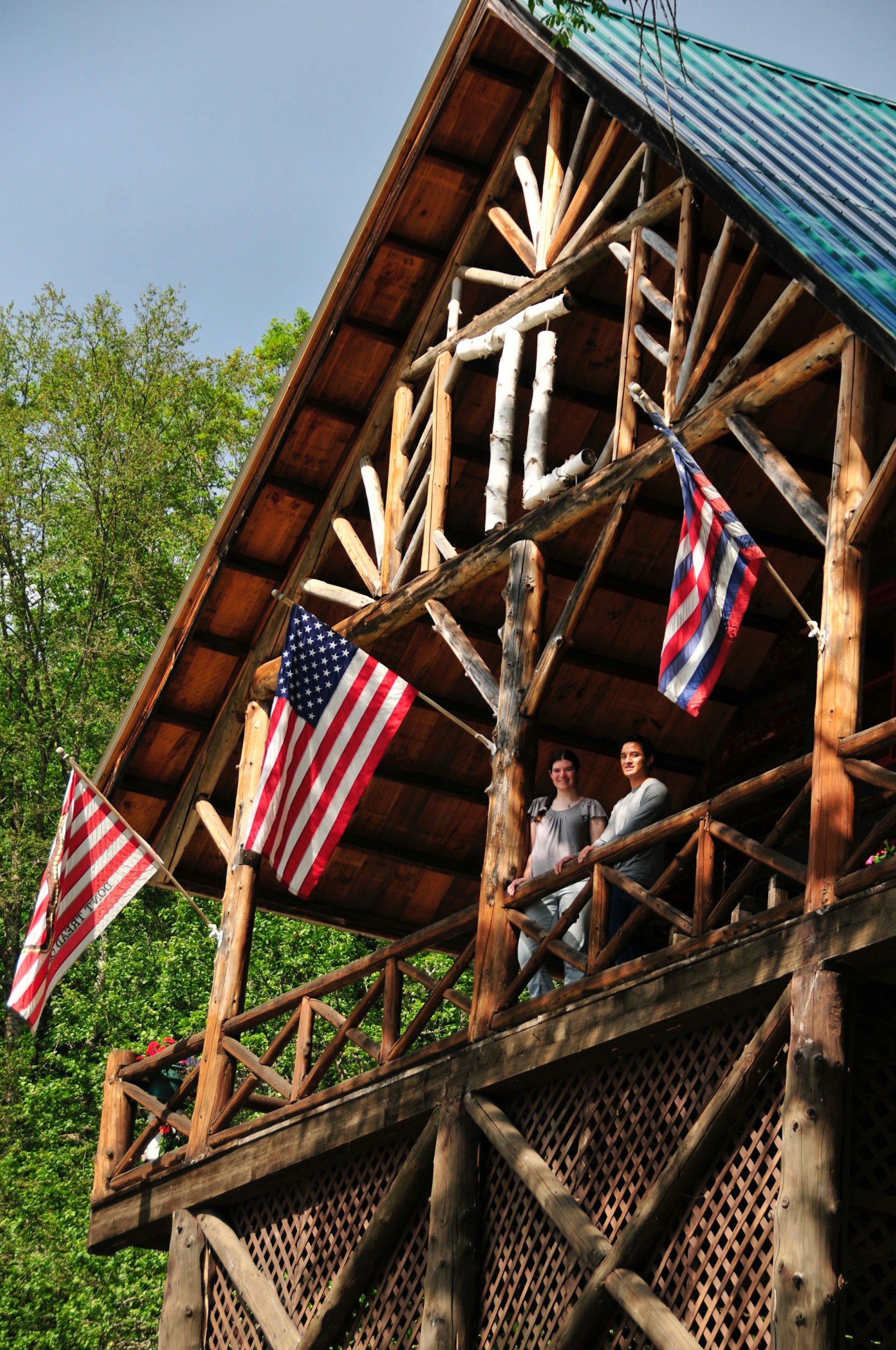Two people look down from the balcony of a log cabin