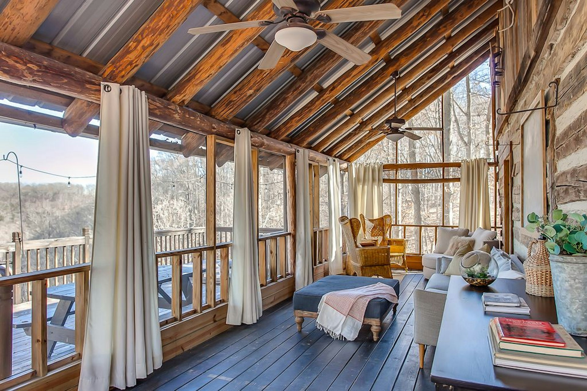 A screened porch with curtains and plush furniture overlooking the woods