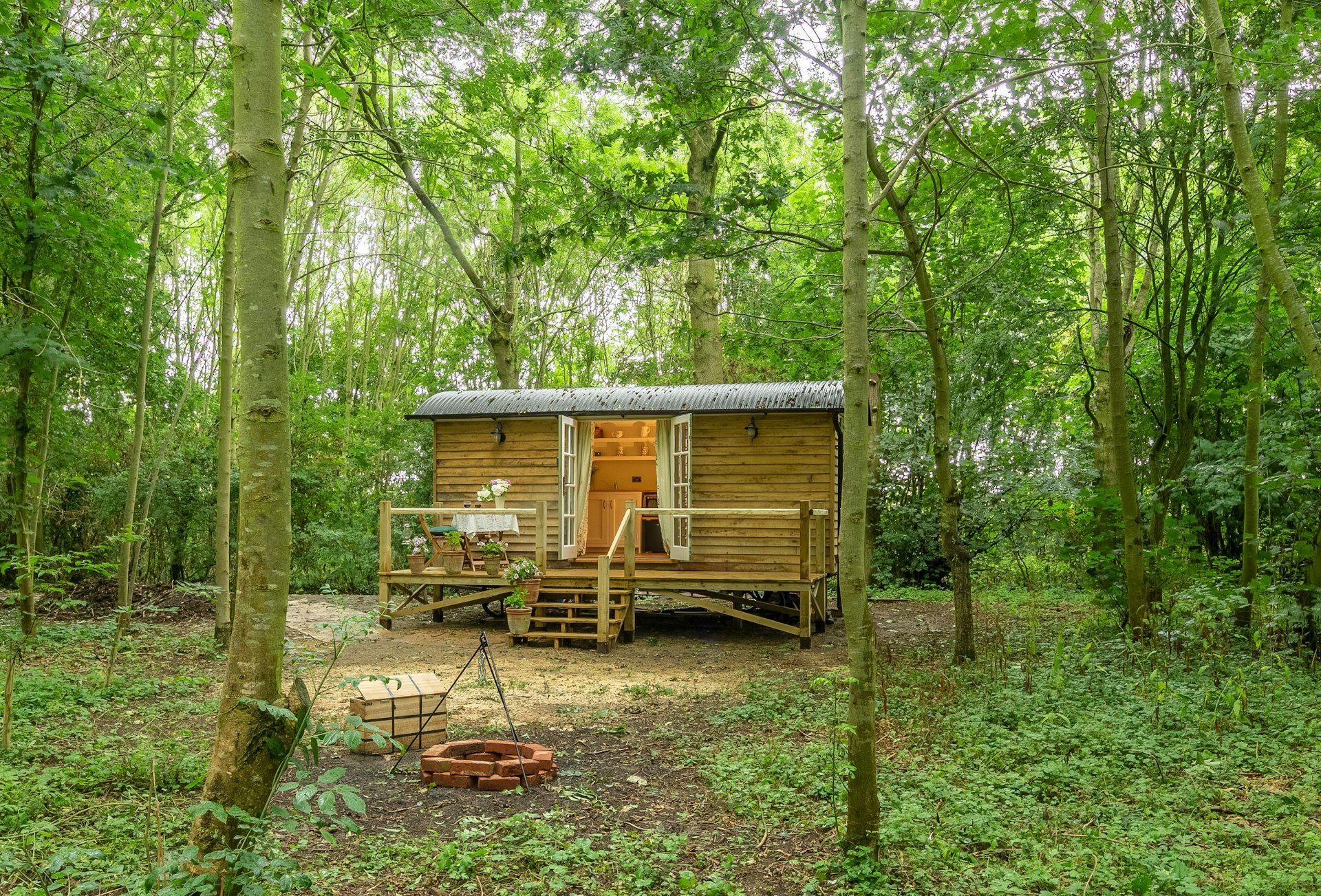 A rustic wood cottage with decking and open double doors in a woodland setting