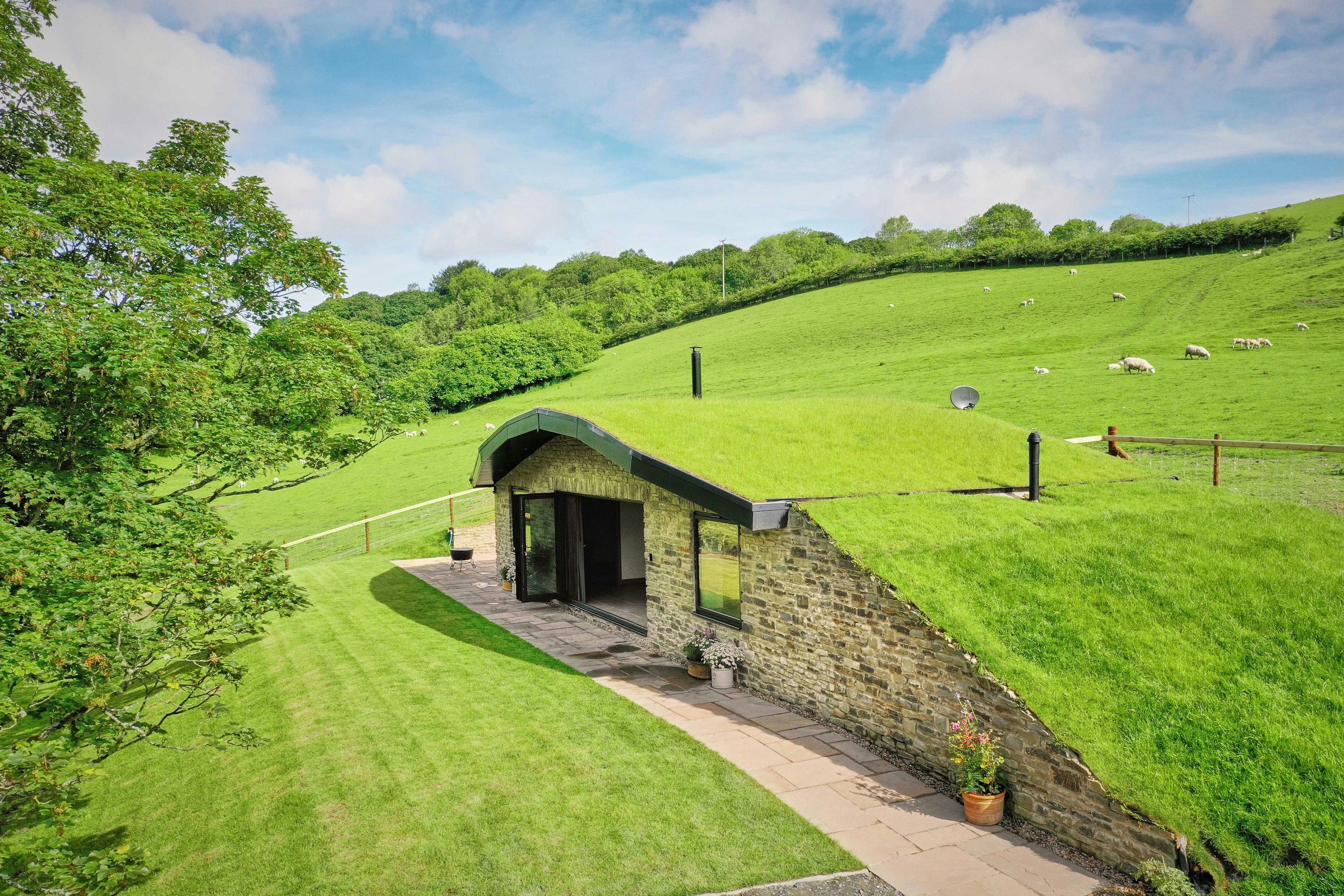 A house with a curved roof covered in grass, blending it in to its surrounding green fields