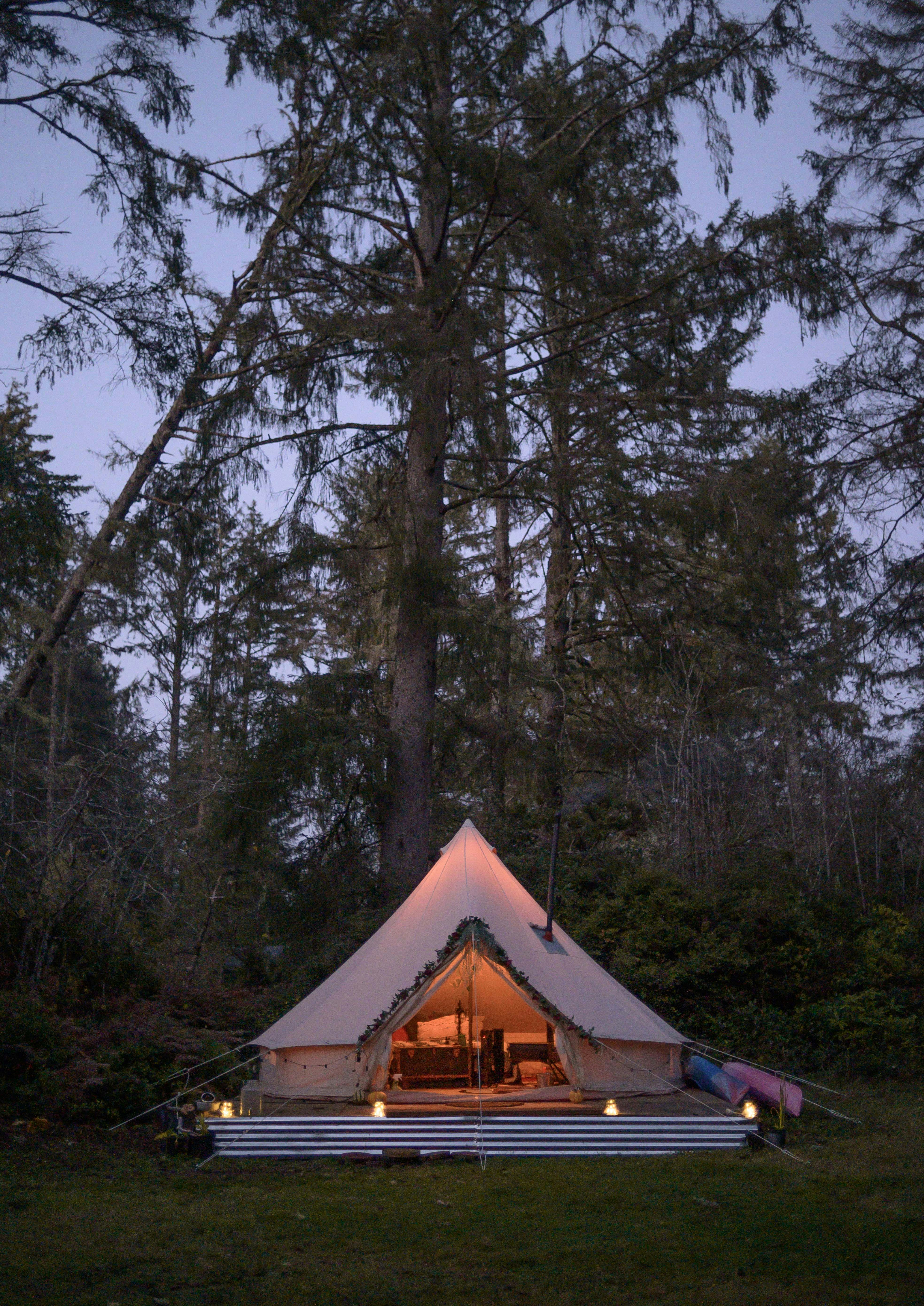 A teepee-style tent on a solid structure surrounded by dense forest at dusk