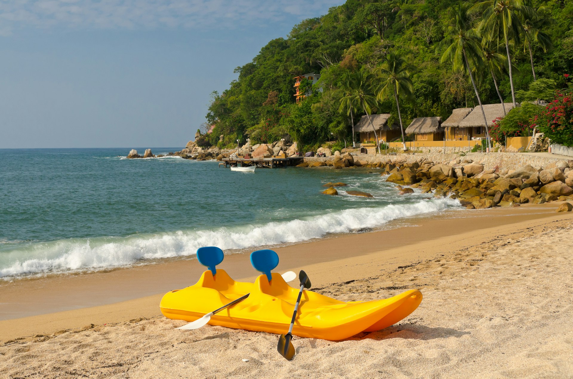 A bright yellow plastic kayak rests on the sand next to the gently lapping waves on a tropical beach in Yelapa, Puerto Vallarta