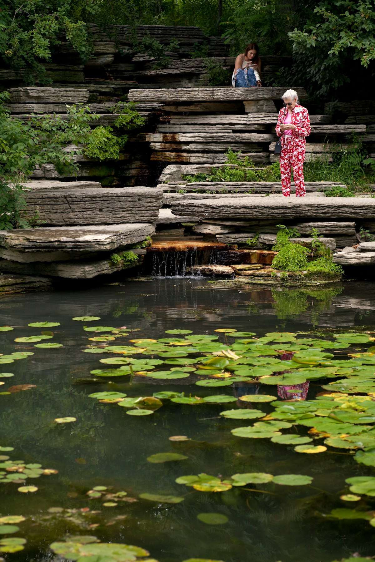 July 29, 2014: Two women check their phones next to the Alfred Caldwell Lily Pool in Lincoln Park Conservatory.