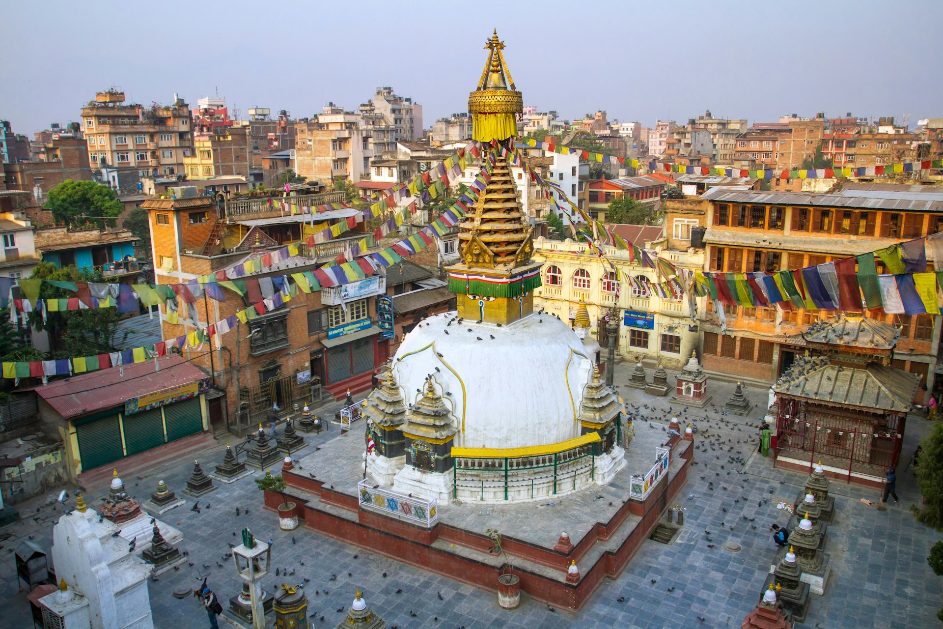 A golden stupa with colorful prayer flags in the centre of an urban area with high-rise buildings