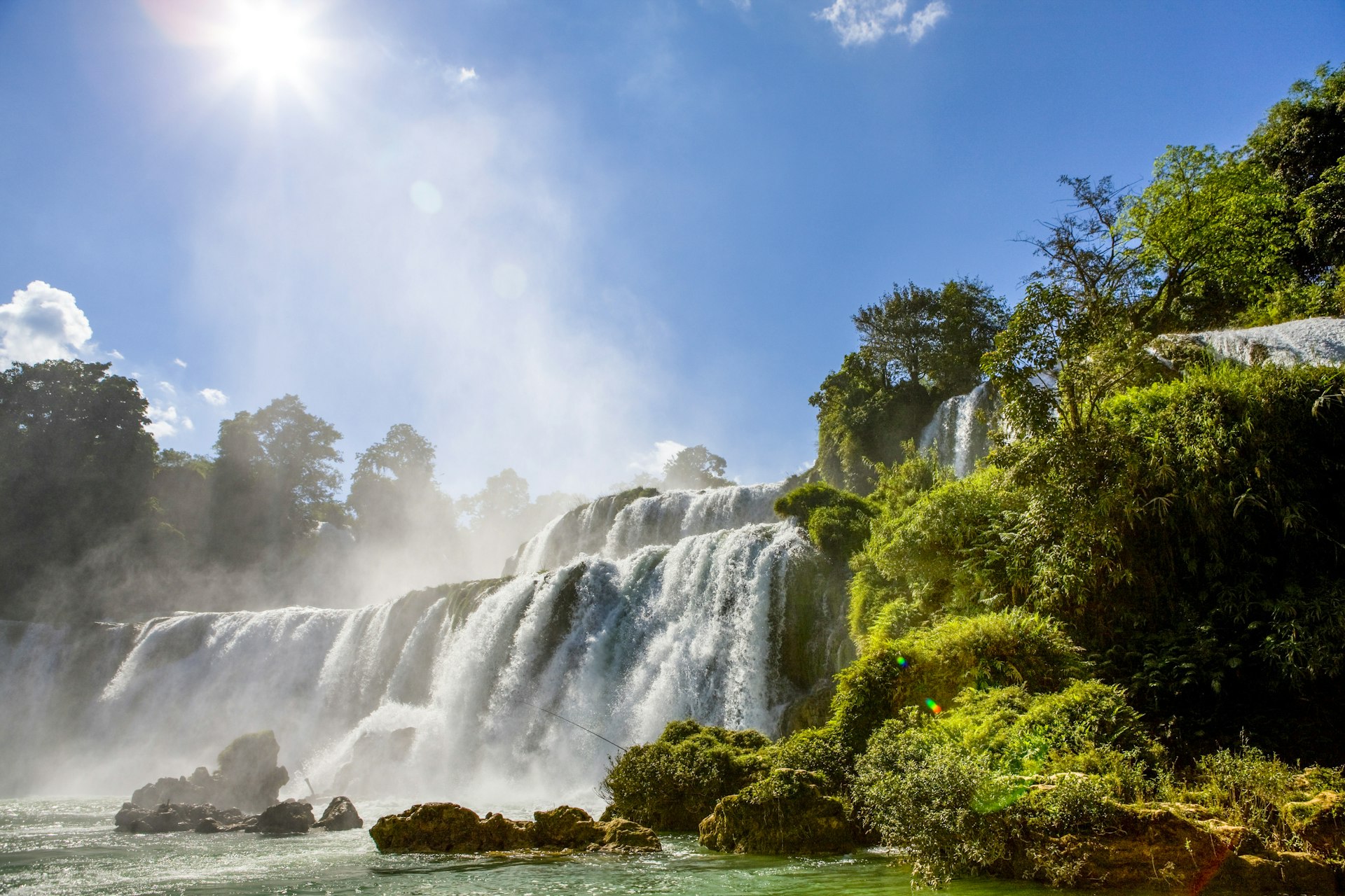 The Ban Gioc Waterfalls flanked by green vegetation on a sunny day.  