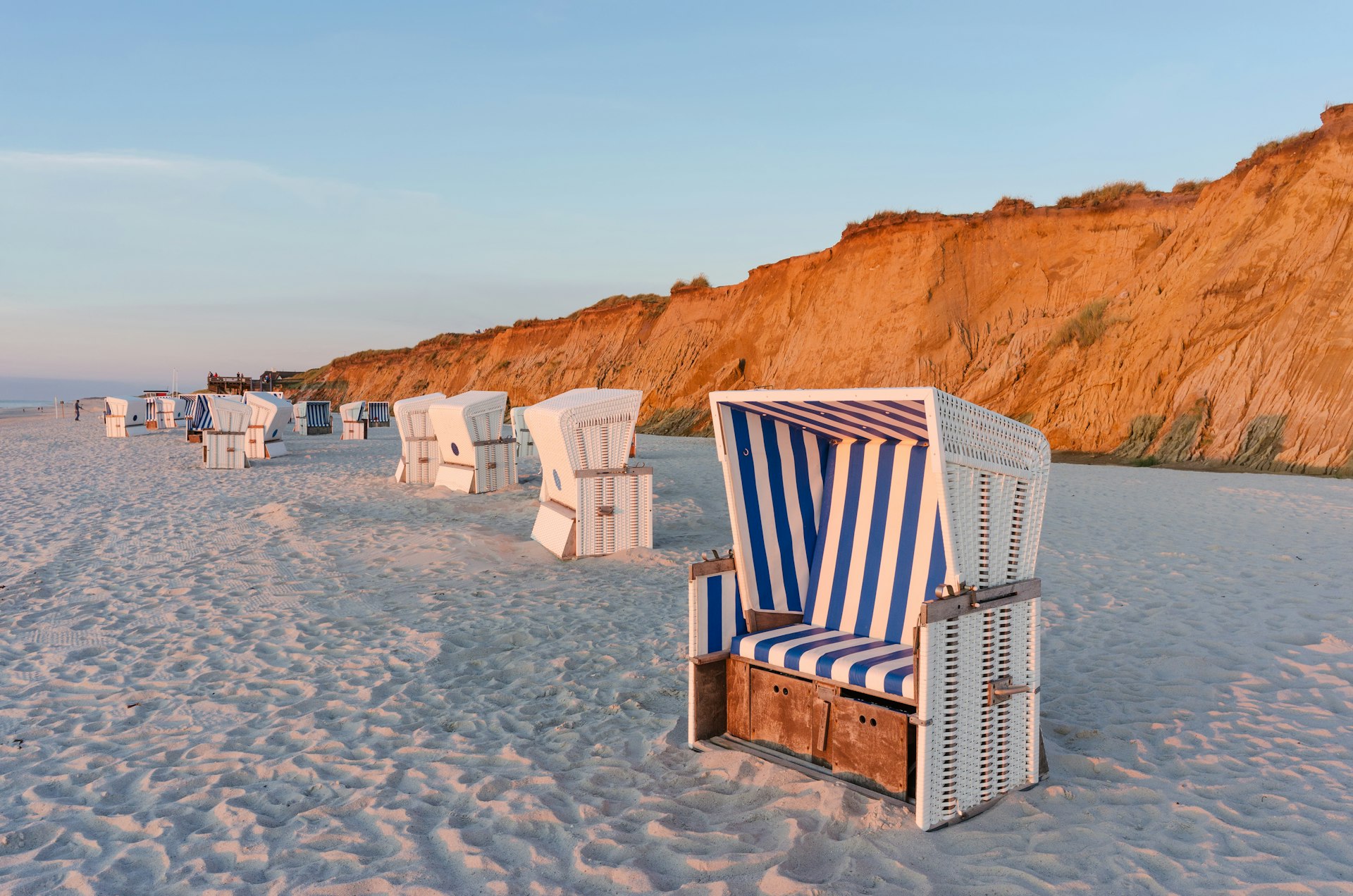 A basket chair, with blue-and-white striped cushions, on a sandy beach