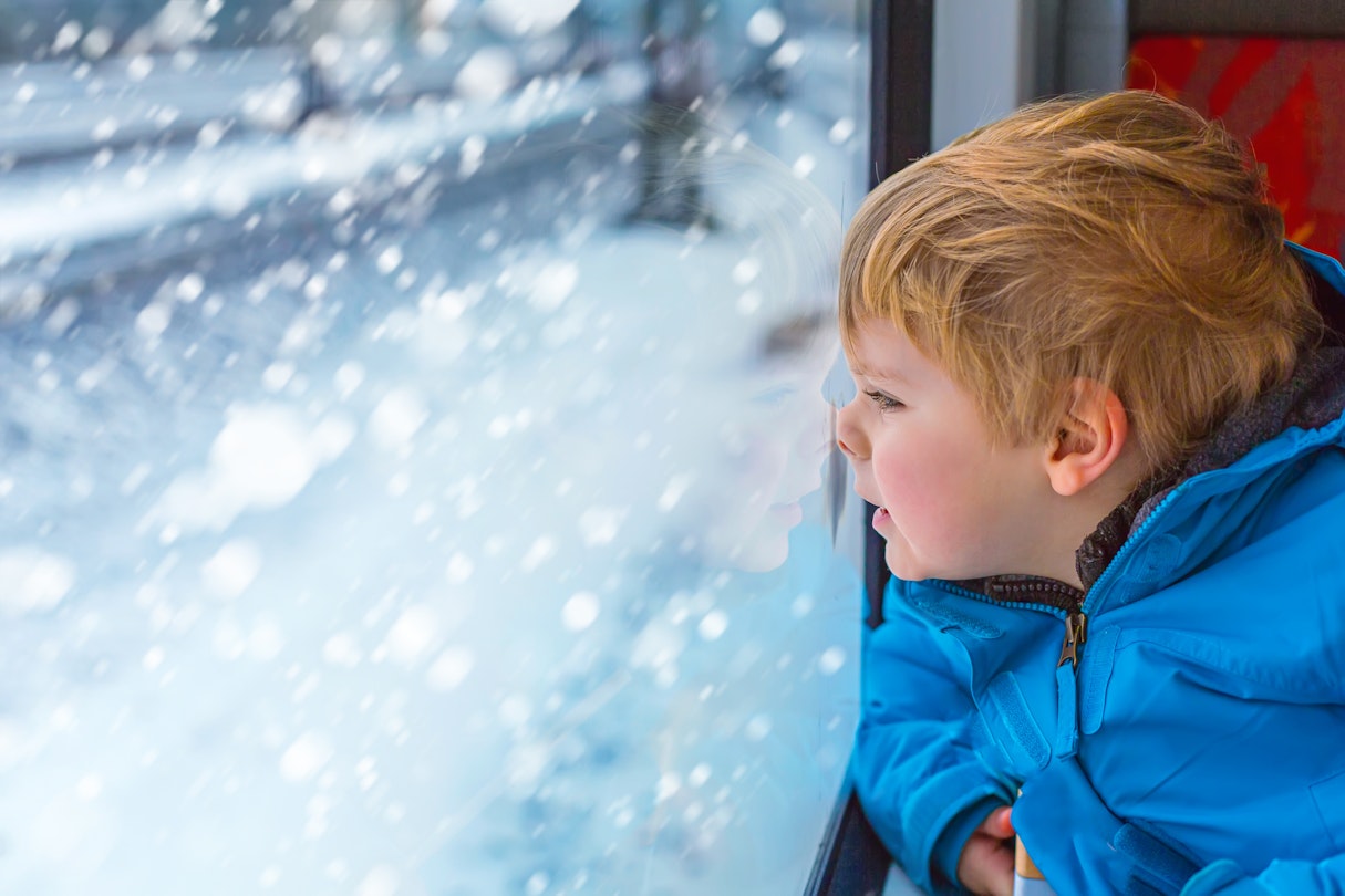 Young boy looking out through the window of a train at a snowy landscape.