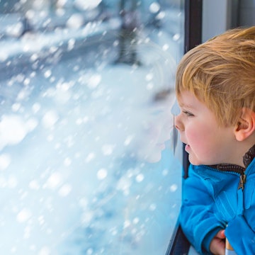 Young boy looking out through the window of a train at a snowy landscape.