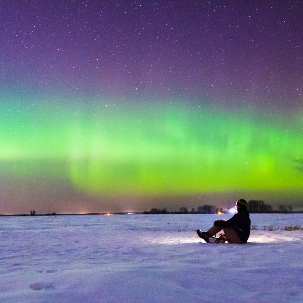 A man sitting on the snow and watching the aurora.