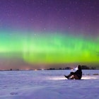 A man sitting on the snow and watching the aurora.