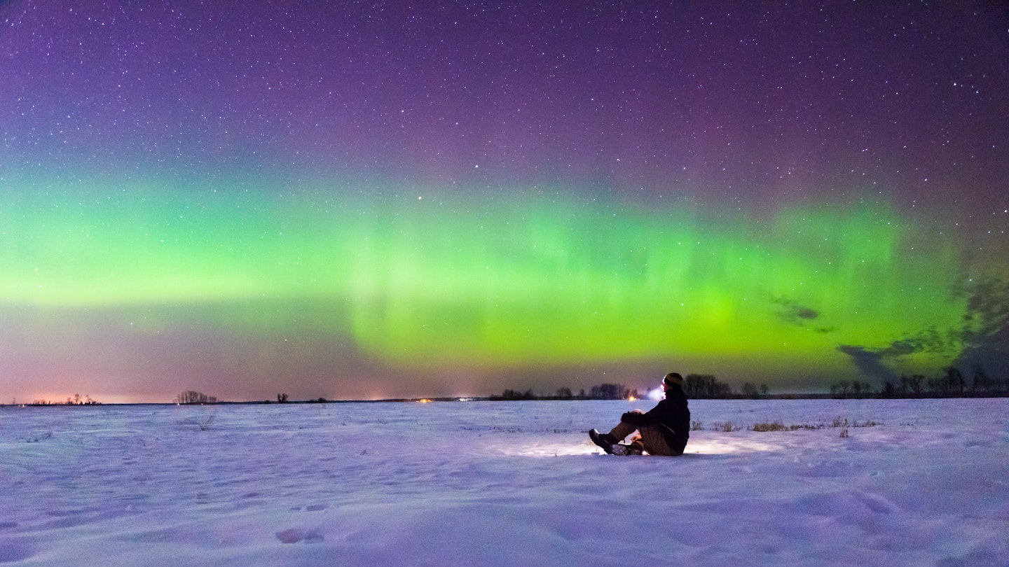 A man sitting on the snow and watching the aurora.