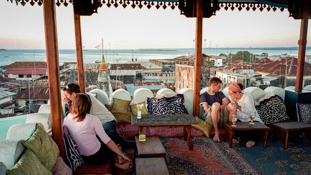 ZANZIBAR, TANZANIA - OCTOBER 6:  (.)  Tourists look towards the sunset while resting on a roof top restaurant at the Emerson & Green Hotel October 6, 2002 in Stone town in central Zanzibar, Tanzania. Zanzibar has become a popular tourist destination due to the beautiful virgin beaches and influence of Arabic, Indian and African cultures on the island.  (Photo by Per-Anders Pettersson/Getty Images)
