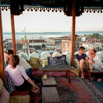 ZANZIBAR, TANZANIA - OCTOBER 6: (.) Tourists look towards the sunset while resting on a roof top restaurant at the Emerson & Green Hotel October 6, 2002 in Stone town in central Zanzibar, Tanzania. Zanzibar has become a popular tourist destination due to the beautiful virgin beaches and influence of Arabic, Indian and African cultures on the island. (Photo by Per-Anders Pettersson/Getty Images)