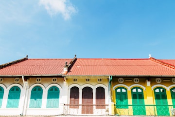 These riverfront French-colonial shophouses in Battambang, Cambodia are characterised by the arcade (five-foot-way), louvered shuttered windows, folding wooden shop doors, a pitched roof, columns and pilaster, and arched windows with shutters. The balcony has elaborate cast-iron works, showing French influences.