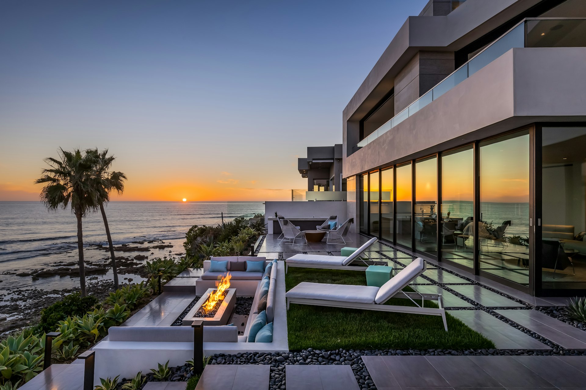 A modern home overlooking the ocean with the sunset reflected in the windows