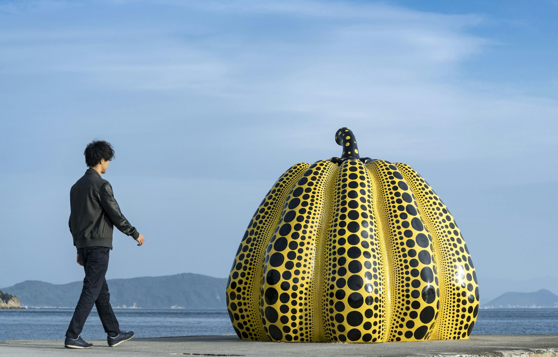 A Japanese tourist approaching Kusama's yellow "Pumpkin" on a pier in Naoshima