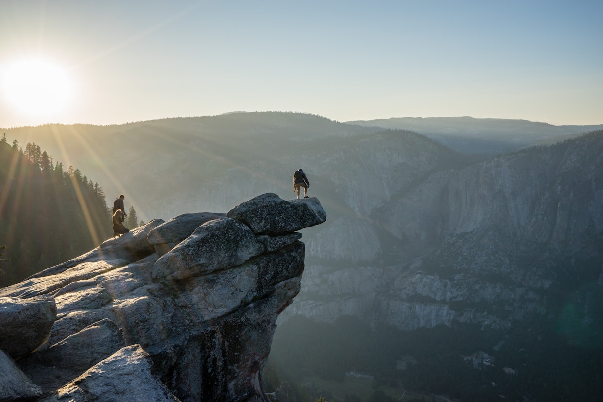 A man stands on the end of the rocky overhang at Glacier point lookout.