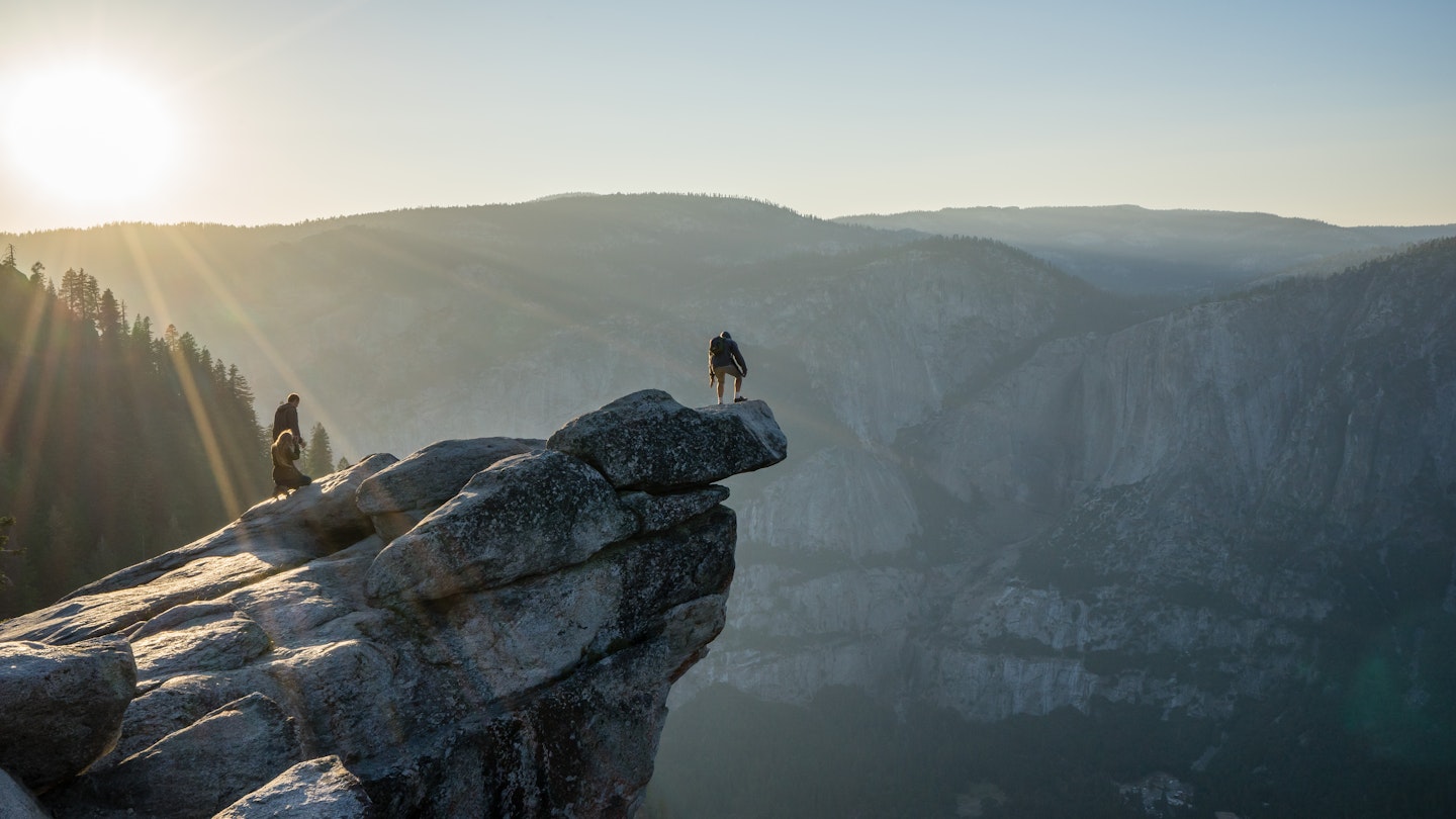 A man stands on the end of the rocky overhang at Glacier point lookout.