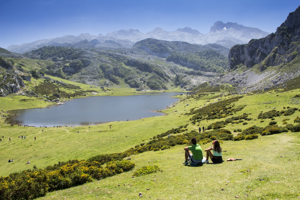 Young couple sitting on the grass overlooking the lakes of Covadonga.