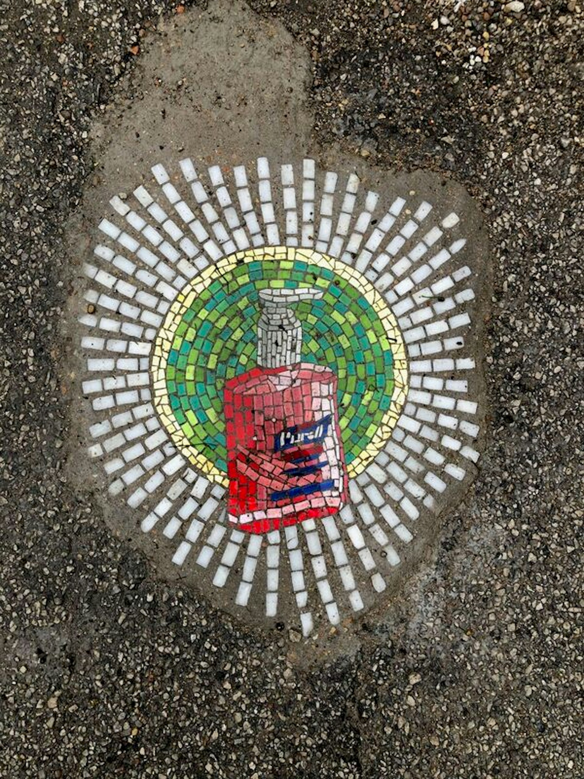 A mosaic depicting a pink bottle of Purell hand sanitizer in a green halo surrounded by white beams of light sits in the pavement of a Chicago pothole
