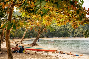 Port Barton, Palawan, Philippines - February 3, 2019: People relax on tropical beach under the lush crown of trees