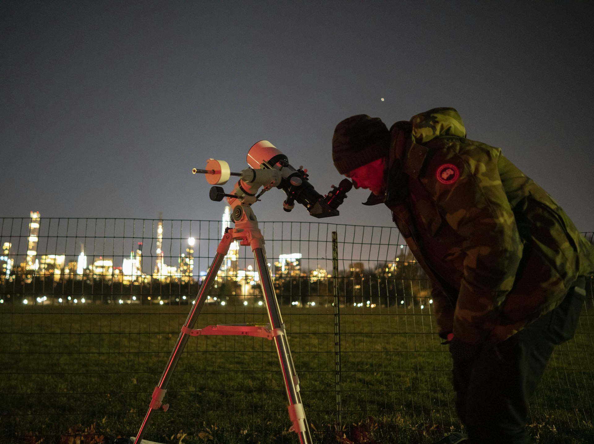 A New Yorker looking through a telescope at night
