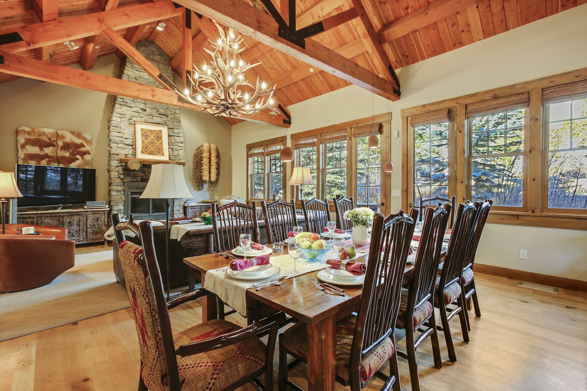 The open-plan living space at Granite Ridge, with a dining table, stone fireplace, and windows looking out on the Tetons