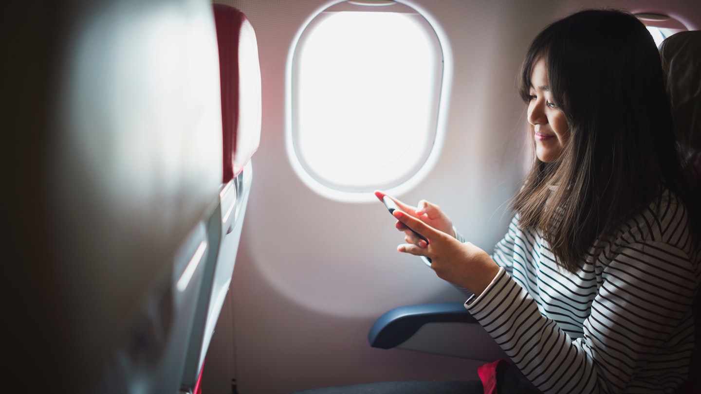 Attractive young asian girl smiles while using smart phone during a commercial flight