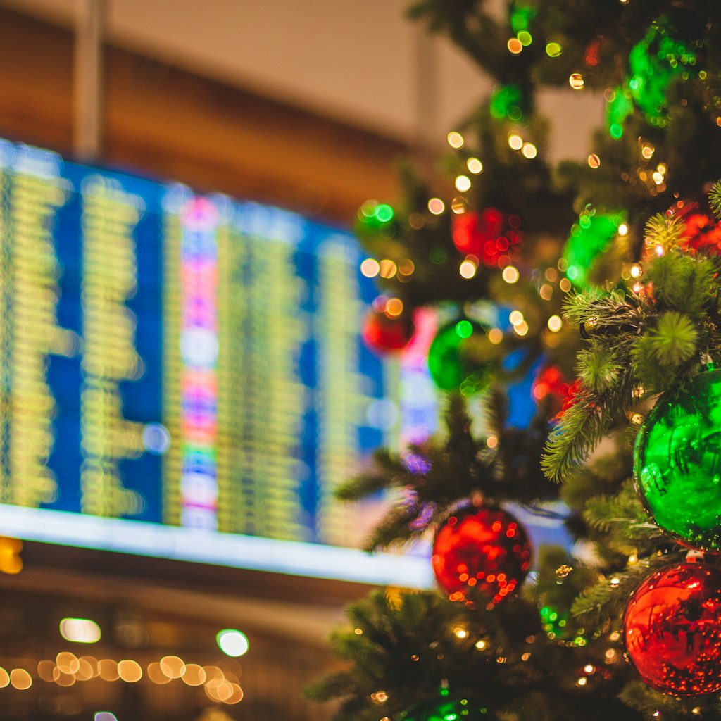 An unrecognizable airport location with a decorated Christmas Tree in the foreground an a flight departures display visible in the background