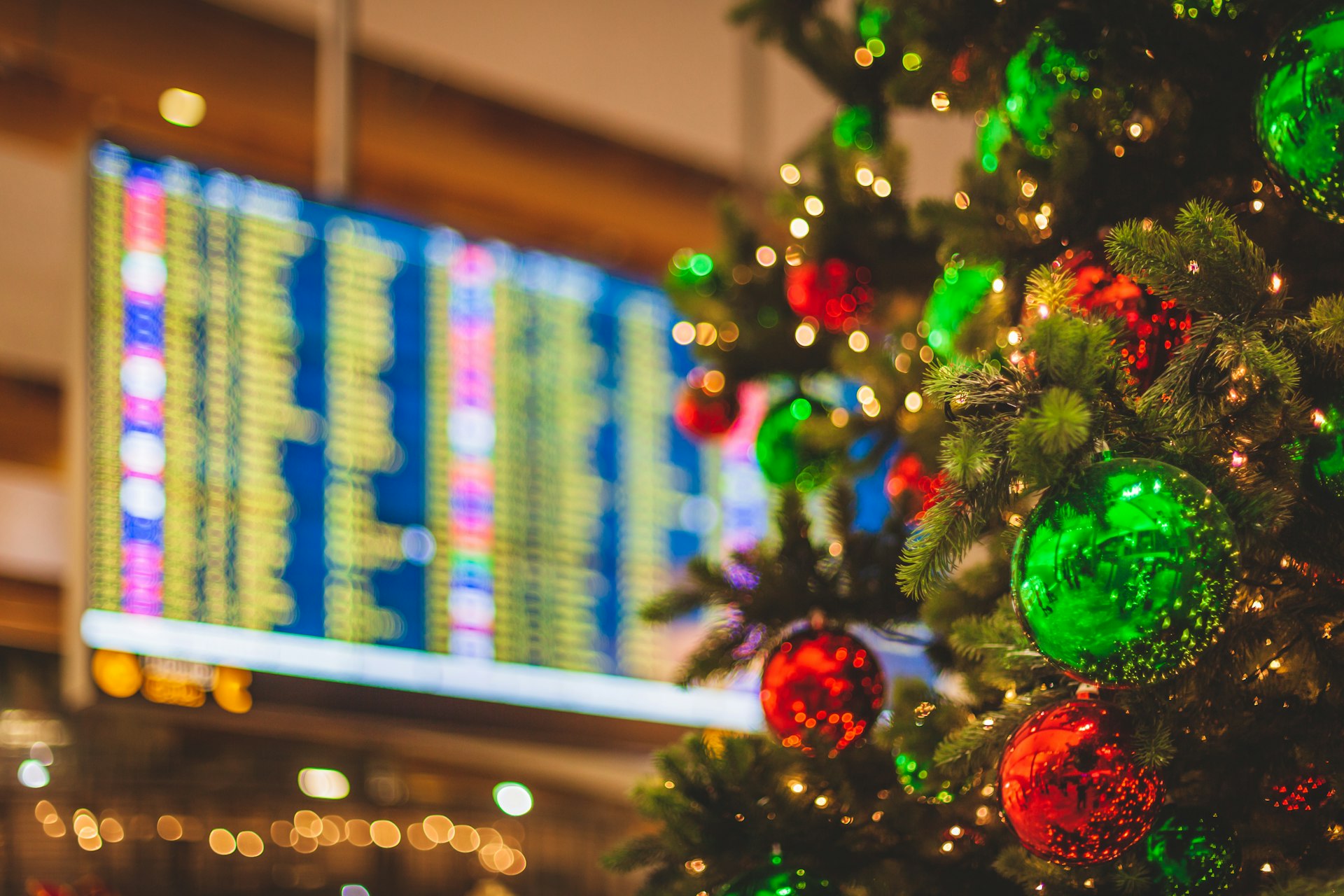 A decorated Christmas tree with a flight departures display in the background