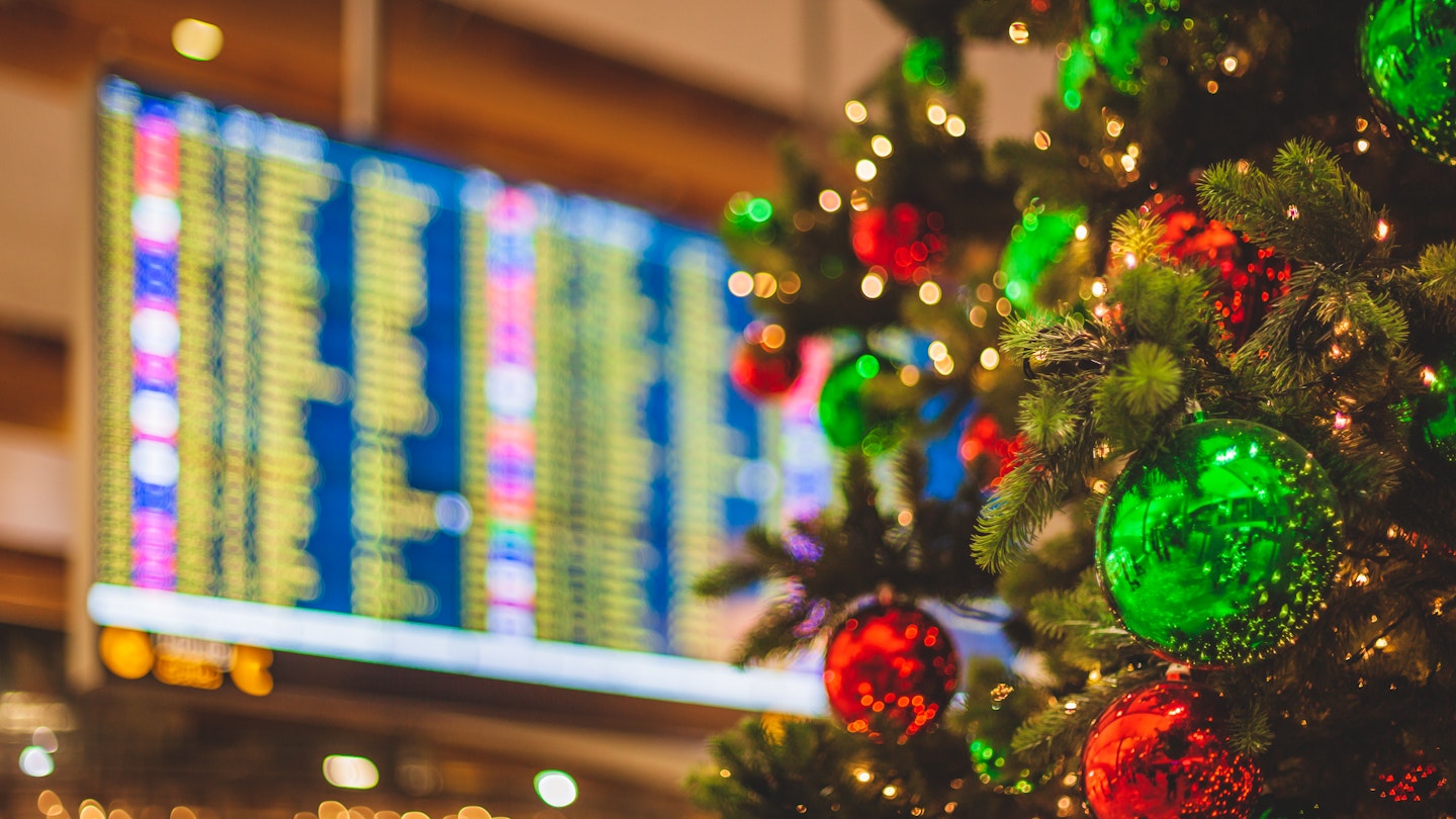 An unrecognizable airport location with a decorated Christmas Tree in the foreground an a flight departures display visible in the background