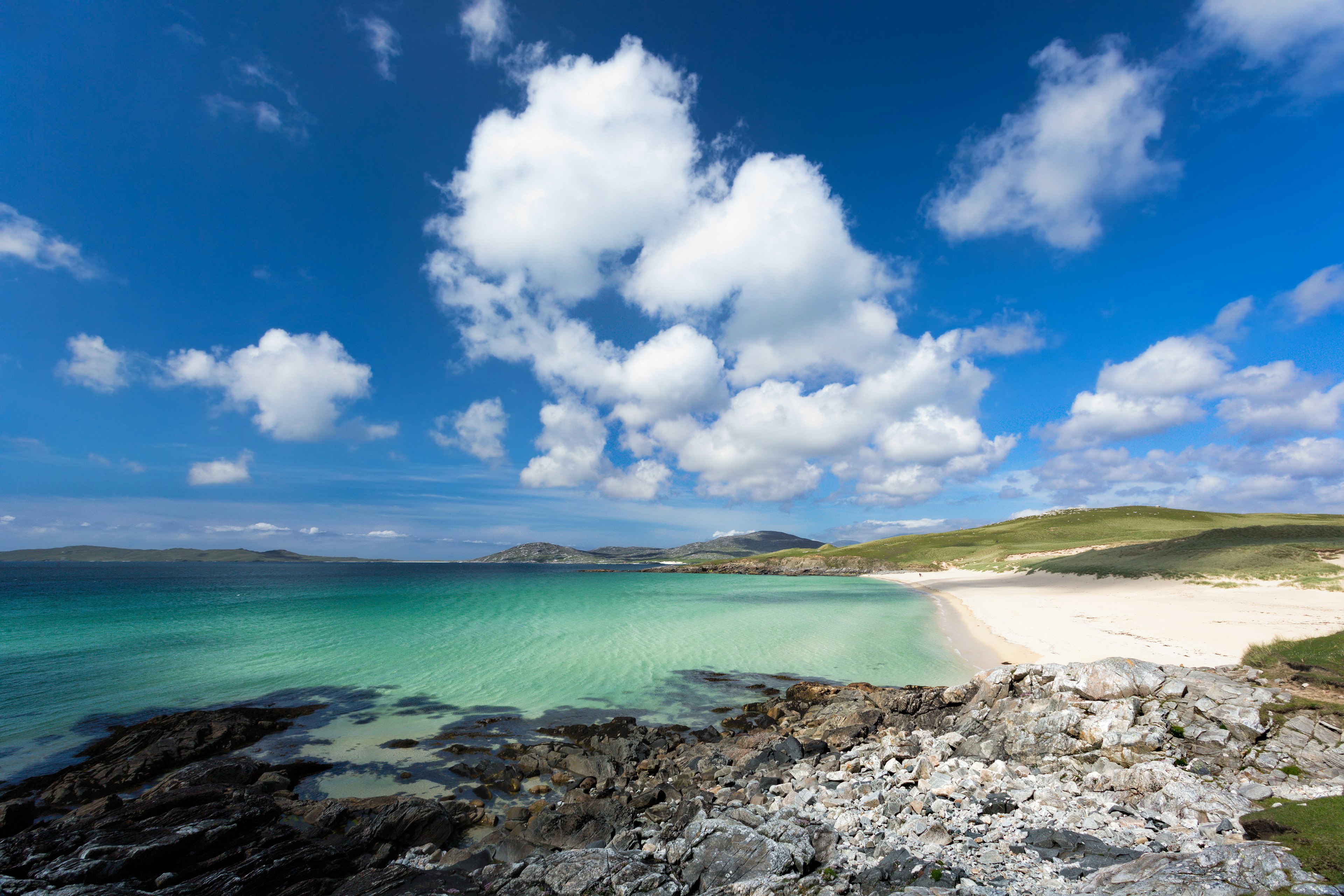 Turquoise waters meet a wide stretch of empty beach on a sunny day.